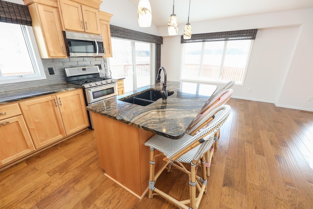 kitchen featuring pendant lighting, sink, a kitchen island with sink, dark stone countertops, and stainless steel appliances