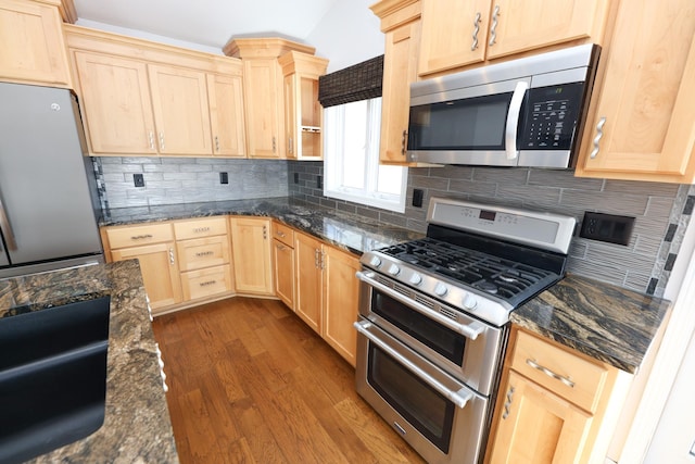 kitchen featuring appliances with stainless steel finishes, hardwood / wood-style floors, light brown cabinetry, tasteful backsplash, and dark stone counters