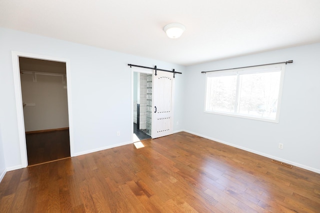 unfurnished bedroom featuring wood-type flooring, a barn door, a closet, and a spacious closet