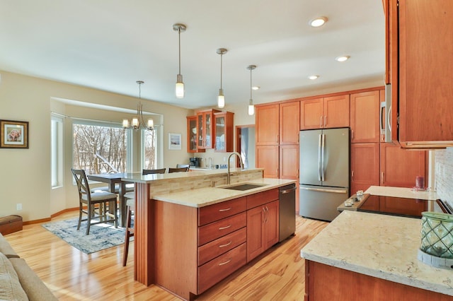 kitchen with light stone counters, appliances with stainless steel finishes, glass insert cabinets, a sink, and a kitchen bar