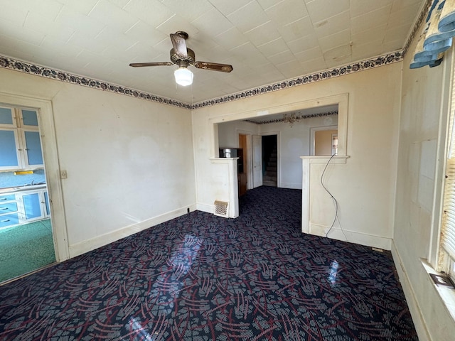 spare room featuring ceiling fan, dark colored carpet, and baseboards