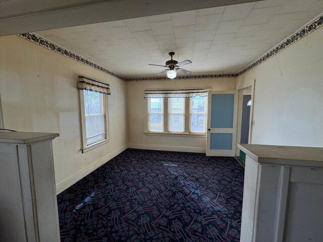 unfurnished room featuring a ceiling fan, dark colored carpet, and baseboards