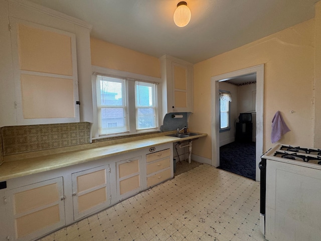 kitchen with dishwasher, gas range, light countertops, light floors, and a sink