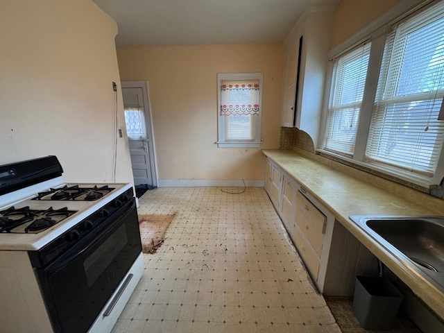 kitchen with range with gas stovetop, light floors, light countertops, a sink, and baseboards