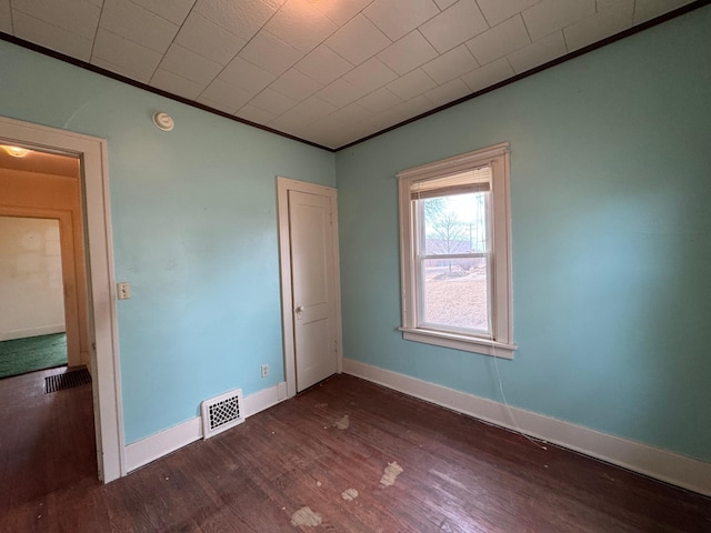 empty room featuring dark wood-style floors, visible vents, crown molding, and baseboards