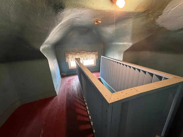 corridor with lofted ceiling, dark wood-type flooring, a textured ceiling, and an upstairs landing