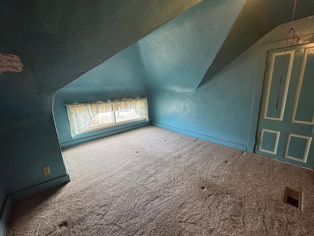 additional living space featuring carpet floors, a textured wall, visible vents, and vaulted ceiling