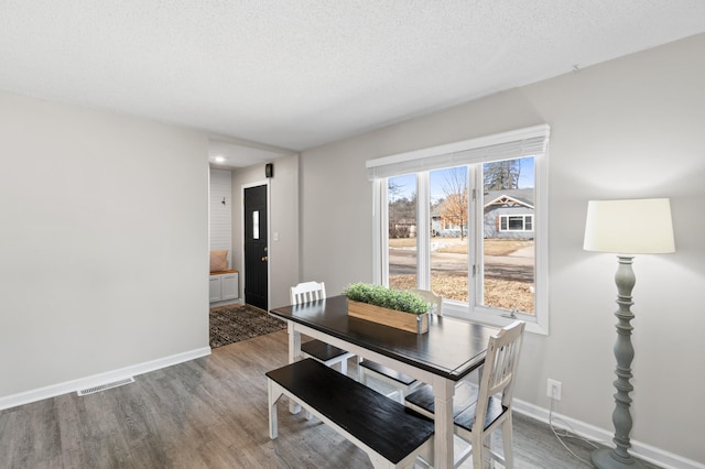 dining space with wood finished floors, baseboards, visible vents, and a textured ceiling