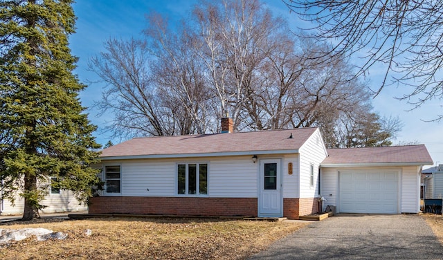 exterior space with aphalt driveway, brick siding, an attached garage, and a chimney