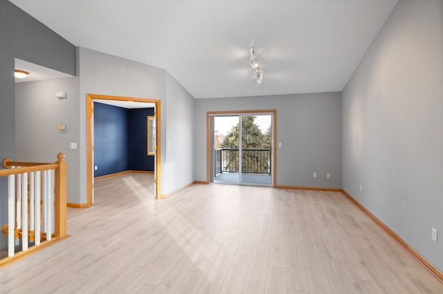 empty room featuring vaulted ceiling, rail lighting, and light wood-type flooring