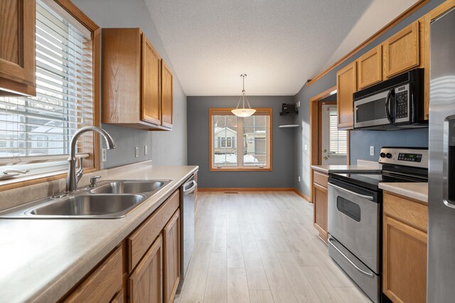 kitchen with pendant lighting, sink, stainless steel appliances, a textured ceiling, and light wood-type flooring