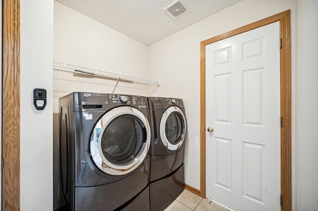 clothes washing area featuring light tile patterned floors, washer and dryer, and a textured ceiling