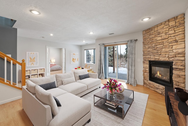 living room featuring a stone fireplace, light hardwood / wood-style flooring, and a textured ceiling