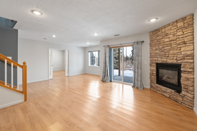 unfurnished living room with a stone fireplace, a textured ceiling, and light hardwood / wood-style floors