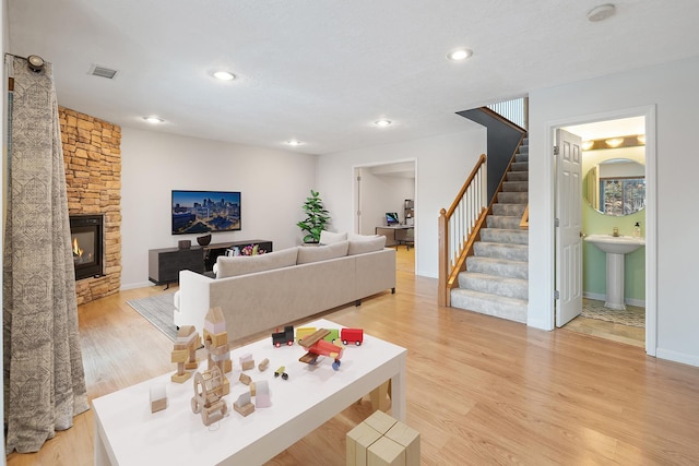 living room with a stone fireplace, sink, and light wood-type flooring