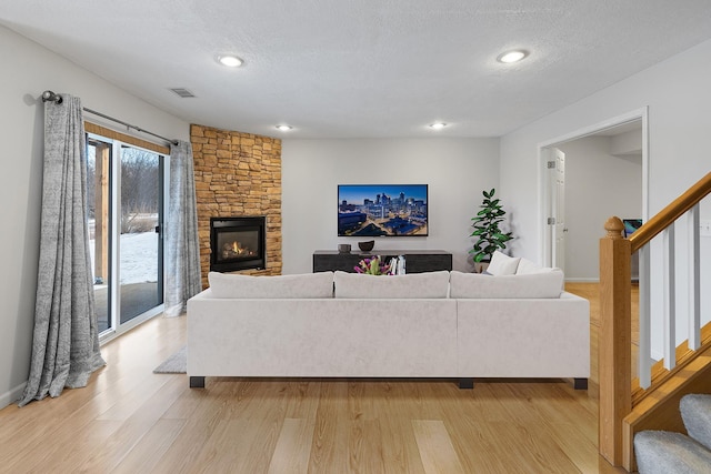 living room featuring a stone fireplace, light hardwood / wood-style floors, and a textured ceiling