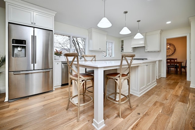 kitchen featuring a center island, light hardwood / wood-style flooring, pendant lighting, stainless steel appliances, and white cabinets