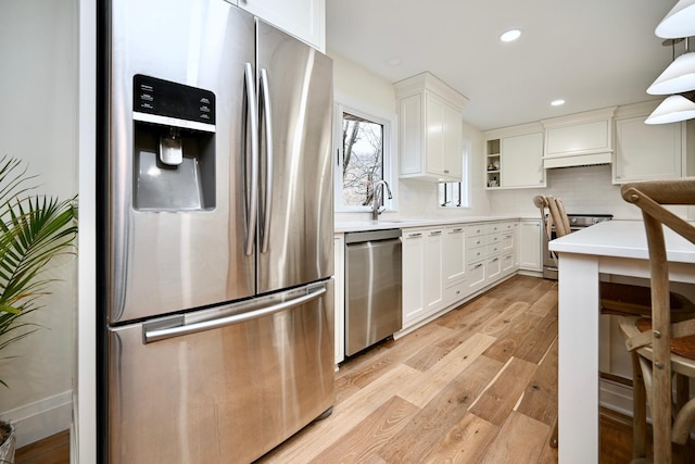 kitchen with stainless steel appliances, hanging light fixtures, white cabinets, and light hardwood / wood-style floors