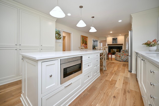 kitchen with pendant lighting, appliances with stainless steel finishes, a fireplace, and white cabinets