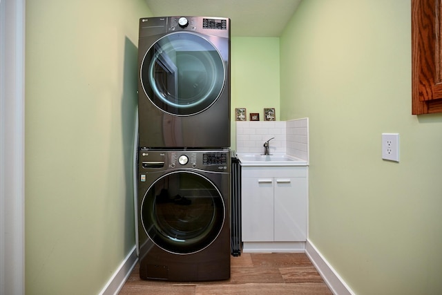 laundry room with stacked washer and dryer, light hardwood / wood-style flooring, cabinets, and sink