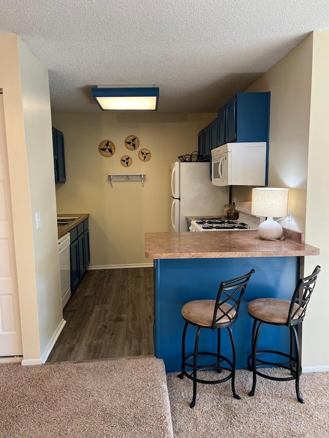 kitchen with white appliances, a kitchen breakfast bar, a peninsula, a textured ceiling, and blue cabinetry