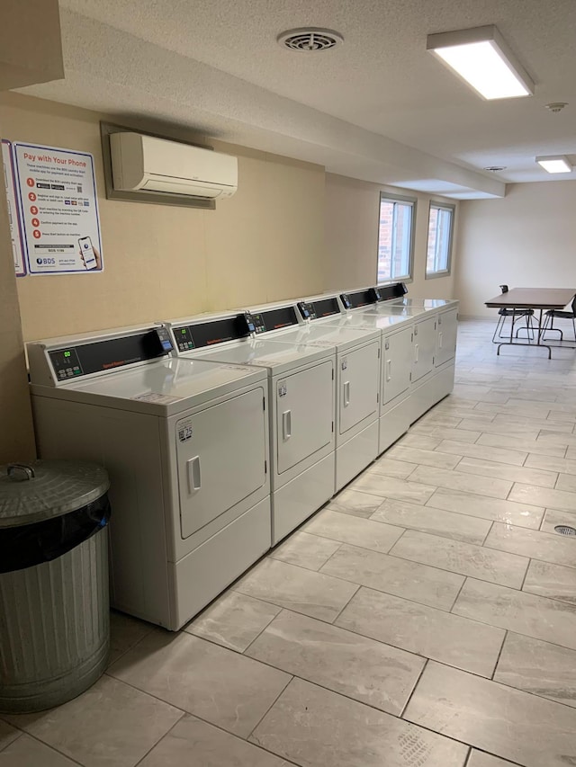 shared laundry area featuring visible vents, a wall unit AC, independent washer and dryer, and a textured ceiling