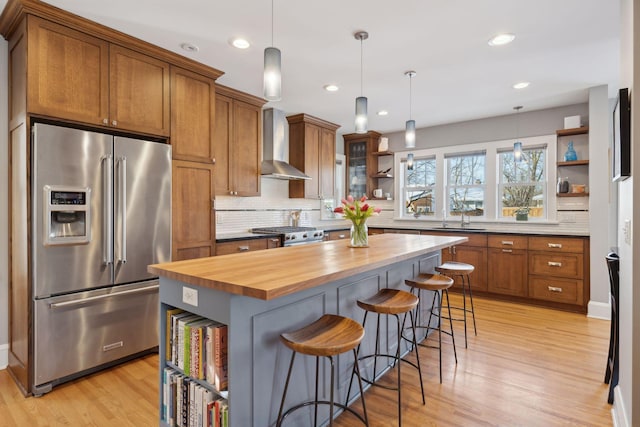 kitchen featuring premium appliances, open shelves, wooden counters, hanging light fixtures, and wall chimney exhaust hood