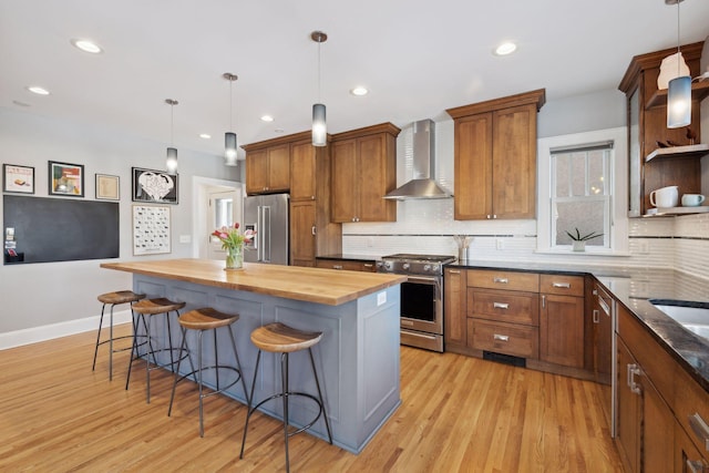 kitchen featuring wall chimney exhaust hood, appliances with stainless steel finishes, a breakfast bar area, and wooden counters