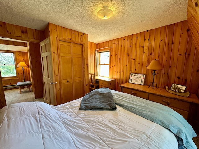 14788 Coyote Dr, Park Rapids, MN 56470 - carpeted bedroom featuring wooden walls, multiple windows, a textured ceiling, a closet, and a baseboard radiator