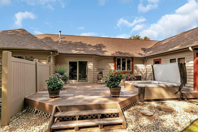 exterior space with fence, a hot tub, a deck, and a shingled roof