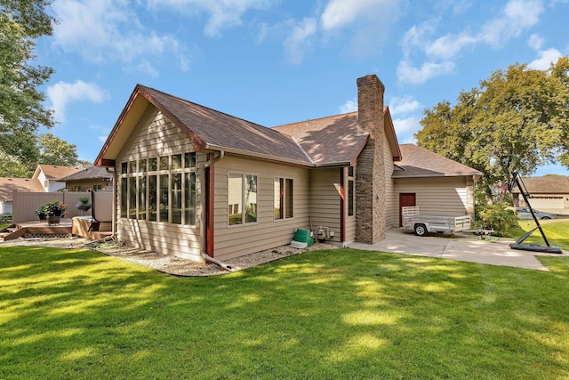 rear view of property featuring a yard, a patio, a chimney, and a shingled roof