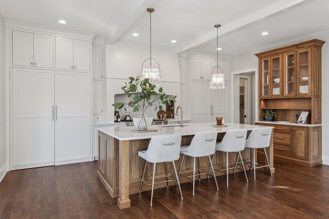 kitchen featuring a large island with sink, dark hardwood / wood-style floors, white cabinets, decorative light fixtures, and beamed ceiling