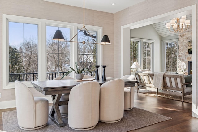 dining space featuring dark wood-type flooring, a stone fireplace, and a chandelier