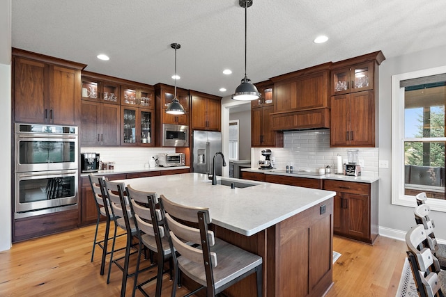 kitchen featuring appliances with stainless steel finishes, pendant lighting, sink, a kitchen bar, and a kitchen island with sink