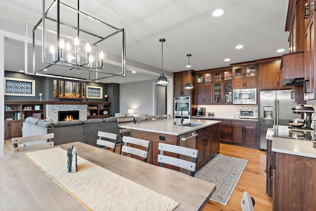 kitchen featuring a fireplace, sink, a kitchen island with sink, stainless steel appliances, and light wood-type flooring