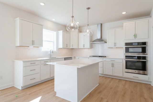 kitchen featuring double oven, stovetop, wall chimney exhaust hood, and light wood-type flooring