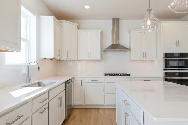 kitchen with a sink, tasteful backsplash, white cabinetry, stainless steel appliances, and wall chimney range hood