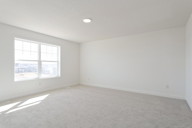 spare room featuring light carpet, visible vents, and baseboards