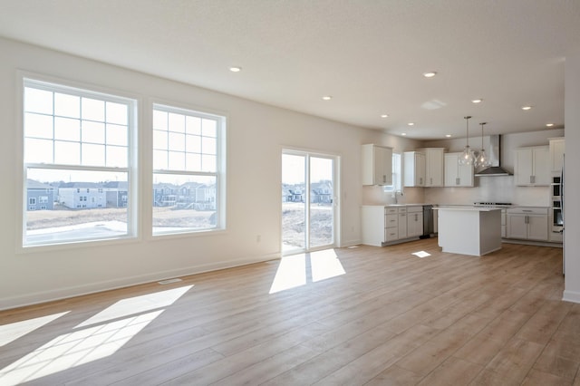 kitchen featuring light wood-type flooring, a sink, a center island, stainless steel appliances, and wall chimney exhaust hood