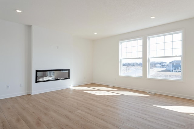 unfurnished living room featuring a glass covered fireplace, baseboards, and light wood finished floors