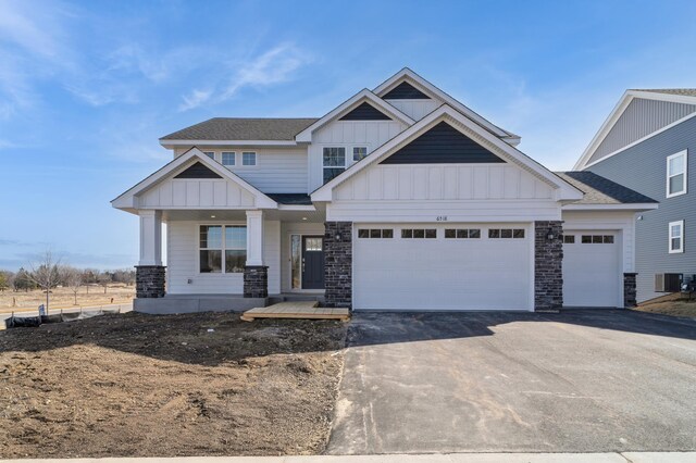 craftsman inspired home with roof with shingles, an attached garage, stone siding, aphalt driveway, and board and batten siding