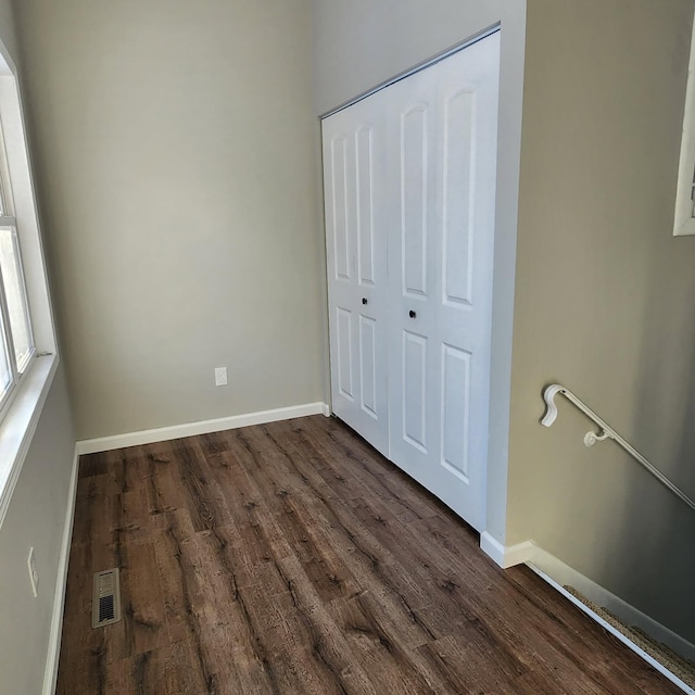 unfurnished bedroom featuring dark wood-style floors, a closet, visible vents, and baseboards