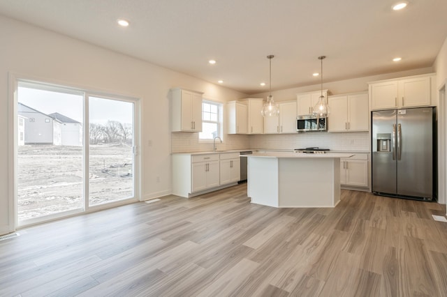 kitchen featuring sink, decorative light fixtures, a center island, stainless steel appliances, and white cabinets