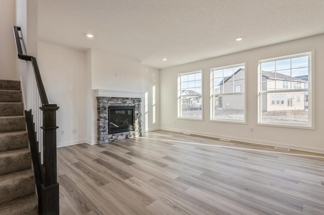 unfurnished living room with a stone fireplace, a textured ceiling, and light hardwood / wood-style floors