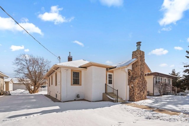 view of front of home with entry steps, a chimney, and stucco siding