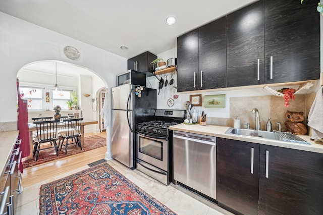 kitchen featuring arched walkways, a sink, light countertops, appliances with stainless steel finishes, and pendant lighting