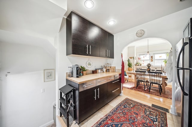 kitchen featuring arched walkways, pendant lighting, visible vents, wooden counters, and freestanding refrigerator