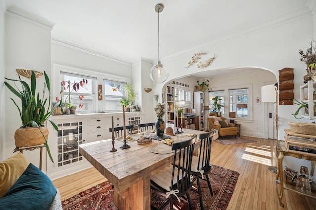 dining area featuring light wood-type flooring, arched walkways, and ornamental molding