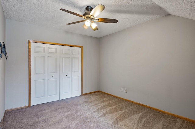 unfurnished bedroom featuring lofted ceiling, a textured ceiling, a closet, ceiling fan, and carpet