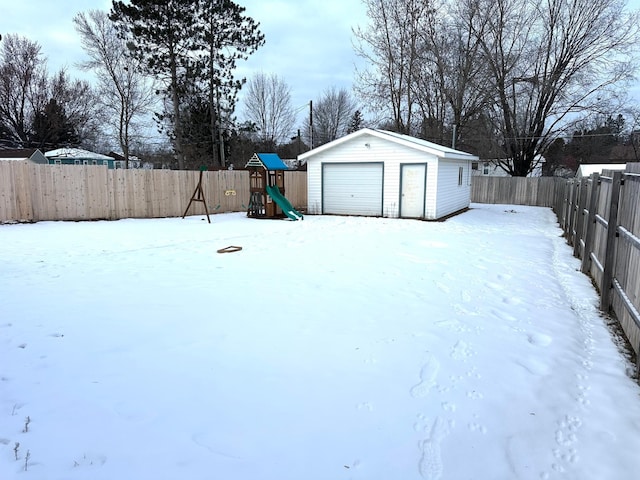 yard layered in snow with a garage, an outdoor structure, and a playground